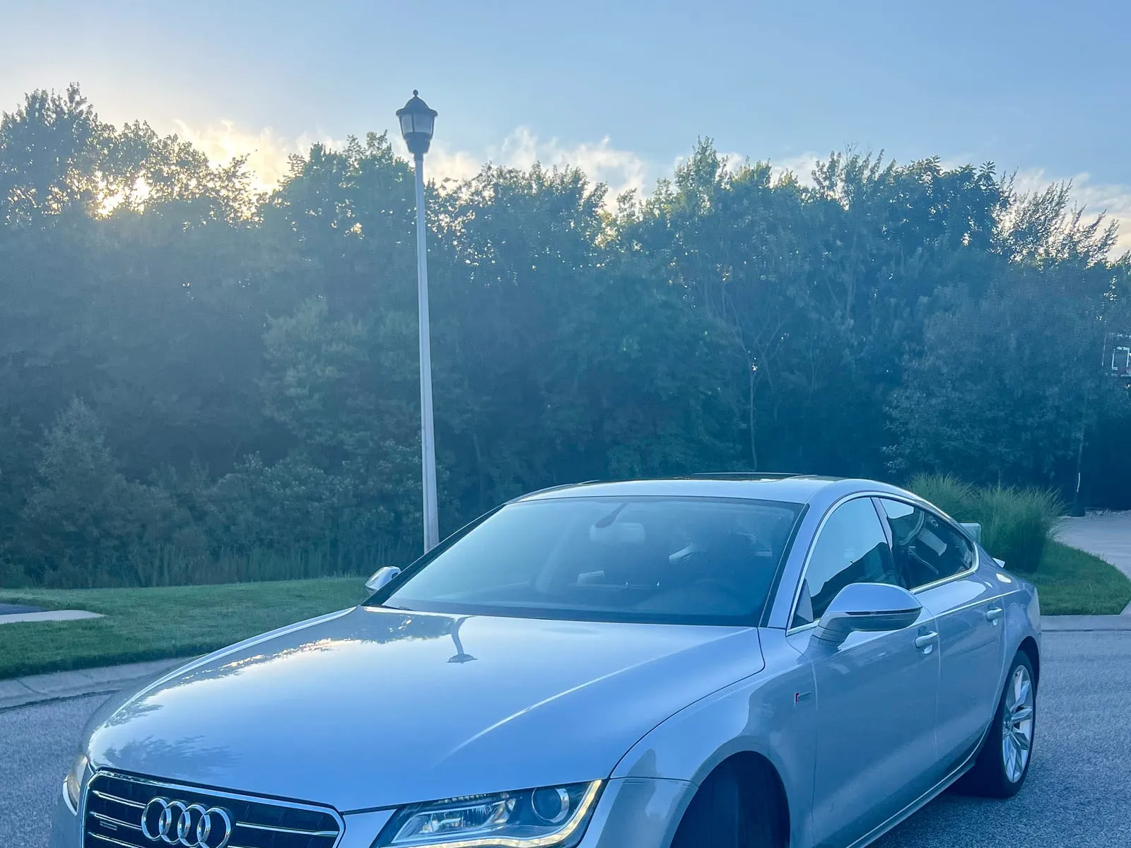 Silver Audi A7 at a three-quarter front angle on a wet driveway, headlights and grille clean