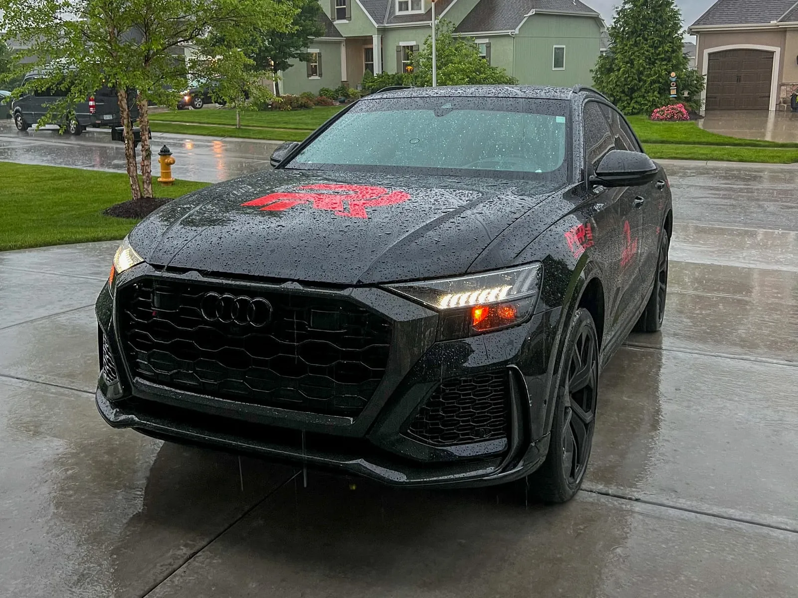 Black Audi RS Q8 at a front three-quarter angle on a wet driveway, mesh grille and headlights cleaned