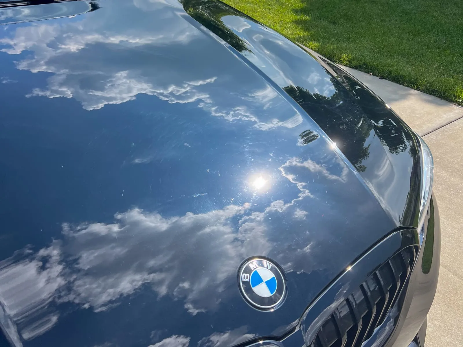 Close view of a black BMW hood and badge reflecting a blue sky and clouds after polishing