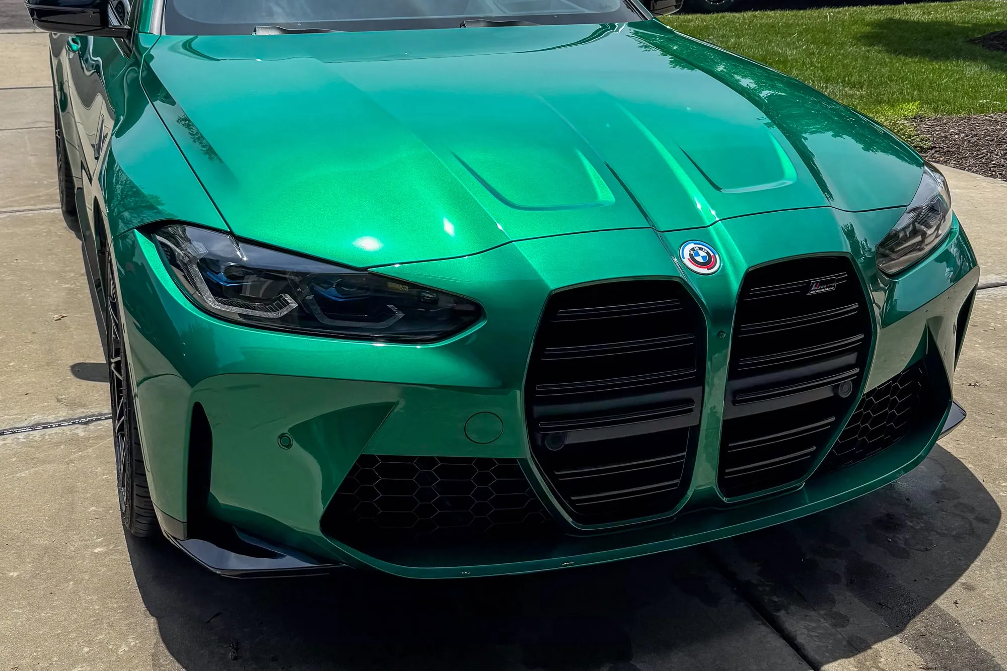 The front of an Isle of Man Green BMW M4 Competition, paint polished to a mirror finish on a driveway