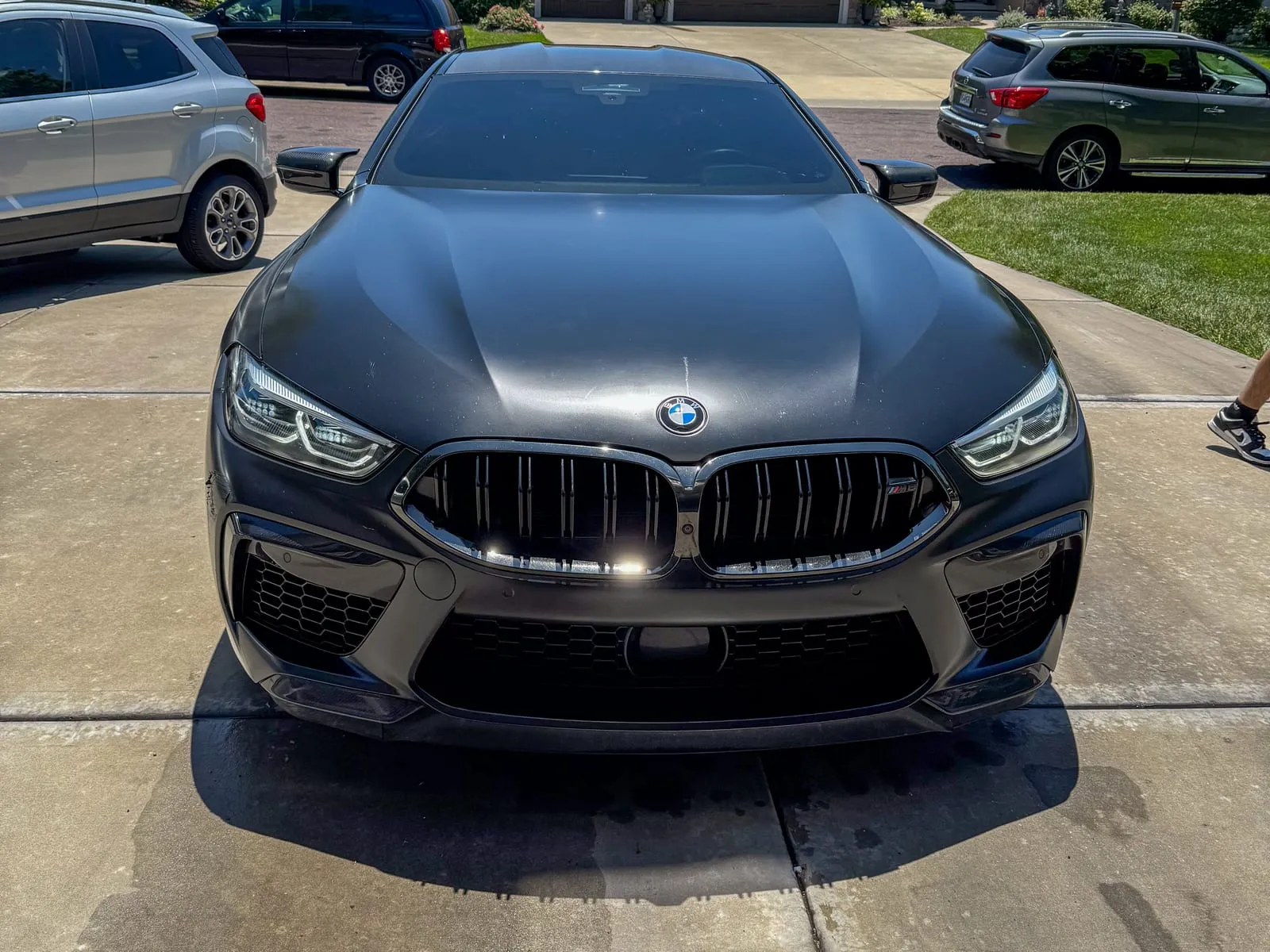 Black BMW M8 Gran Coupe head-on in a driveway, grille and headlights clean and the paint still wet