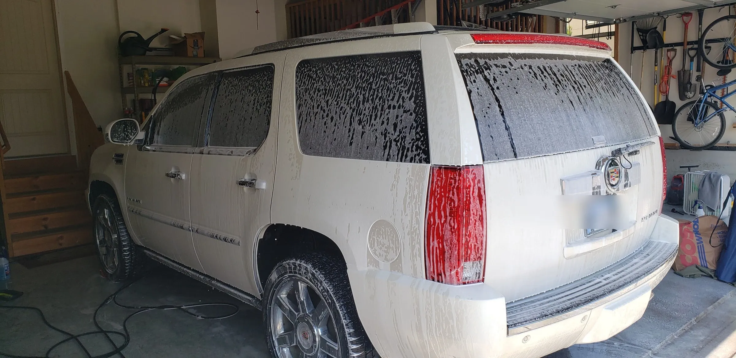 White Cadillac Escalade covered in wash foam inside a garage, before rinsing