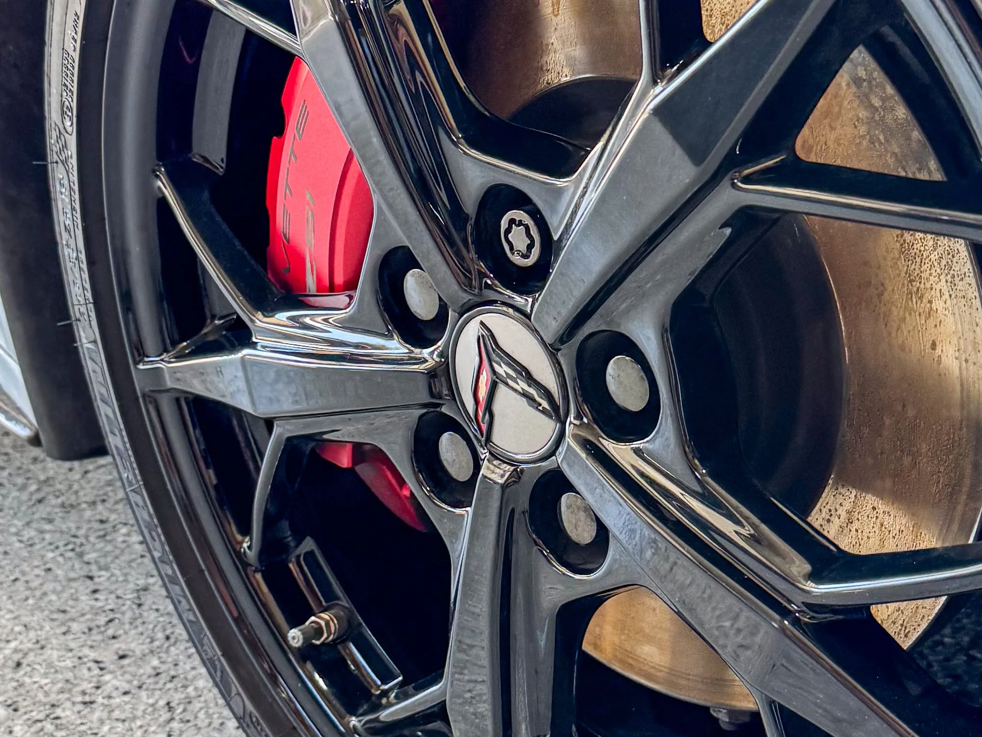 The same C8 Corvette wheel after decontamination, gloss black with a red caliper behind the spokes