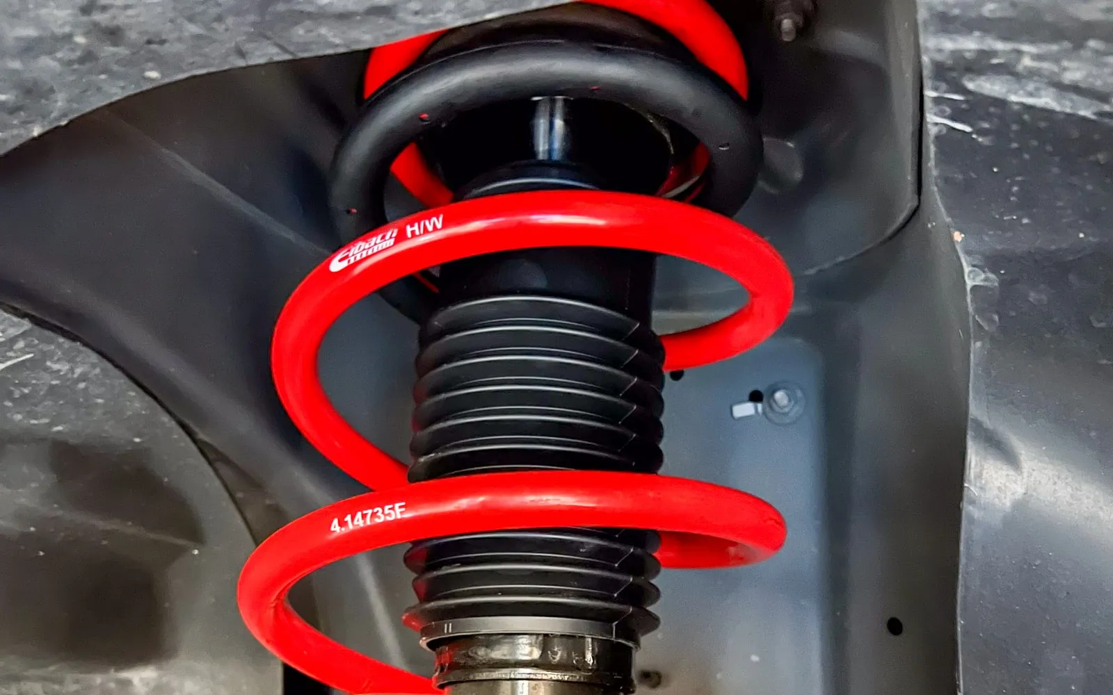 A red lowering spring installed on a strut, viewed from underneath the wheel well