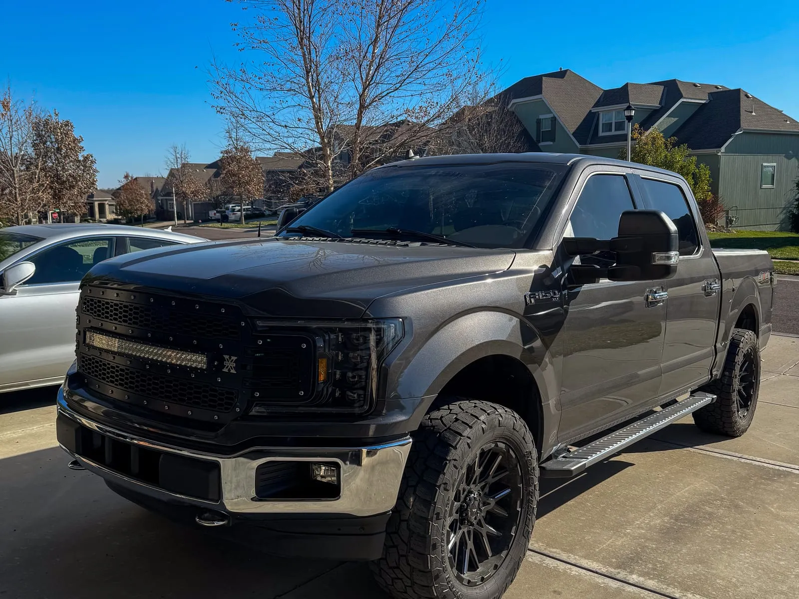 Black lifted Ford F-150 on knobby tires parked on a driveway, body and wheels washed