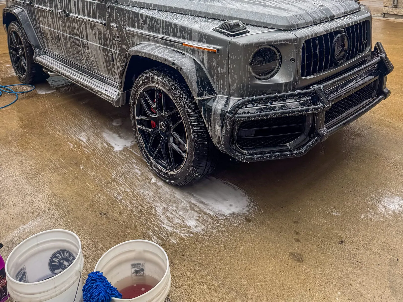 Mercedes-AMG G63 covered in wash foam on a driveway, wheels and arches still soaking