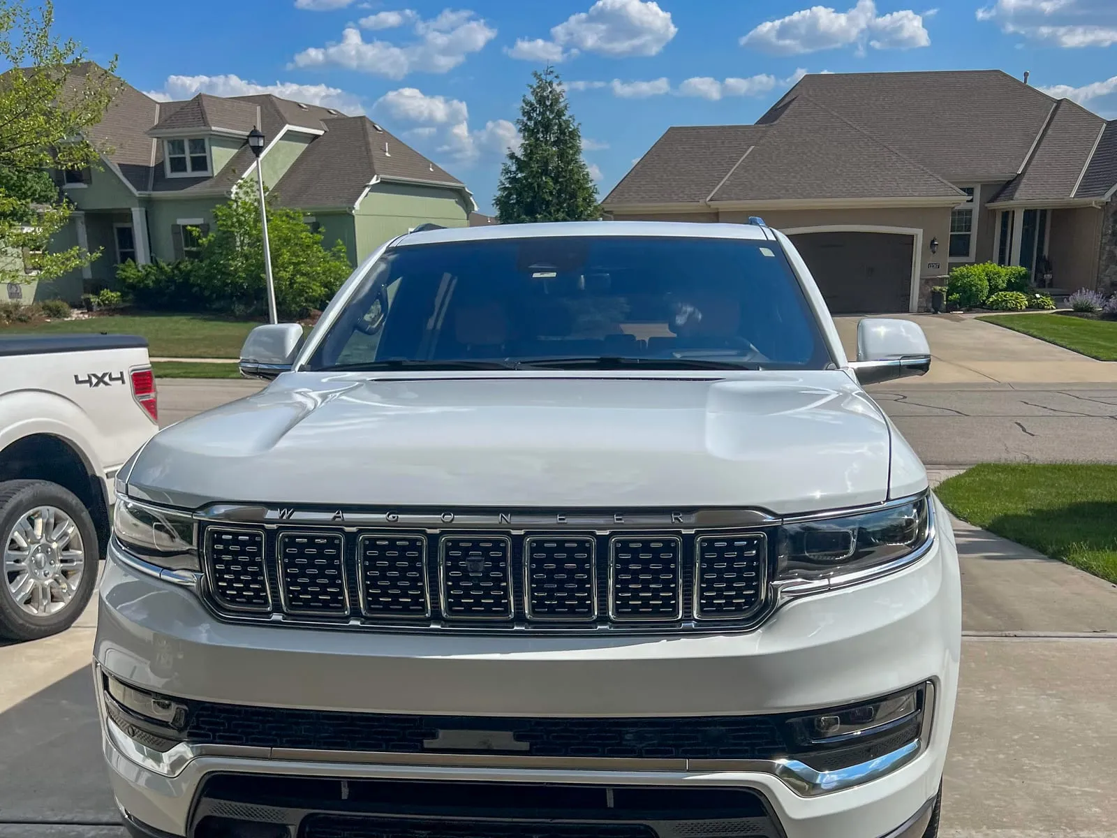 White Jeep Grand Wagoneer head-on in a driveway, the full-width grille cleaned