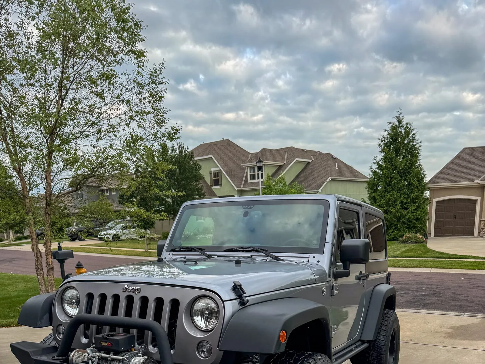 Grey Jeep Wrangler with a front winch bumper on a driveway, tires dressed and body washed