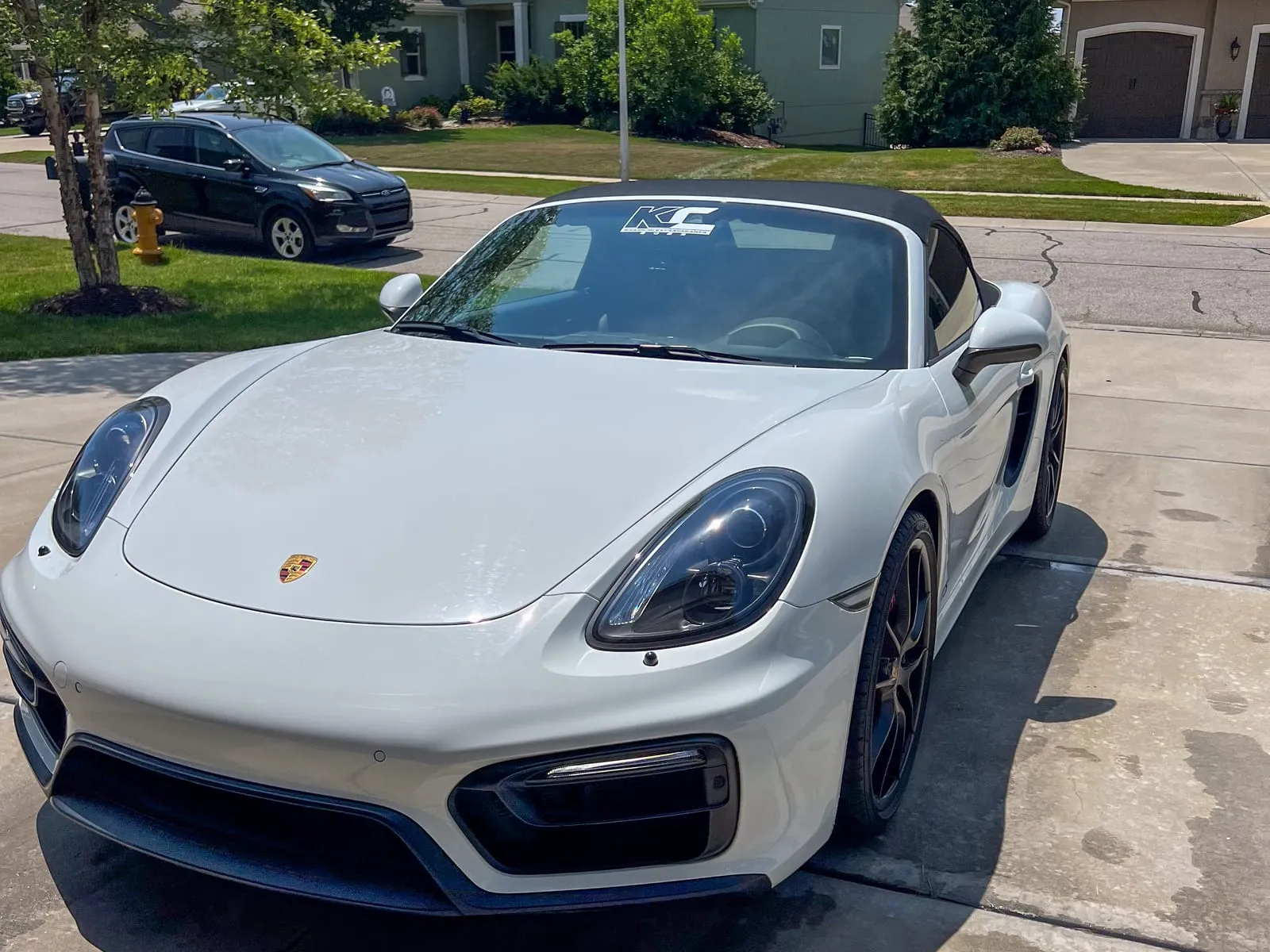 White Porsche 718 Boxster with the roof down on a driveway, black wheels cleaned