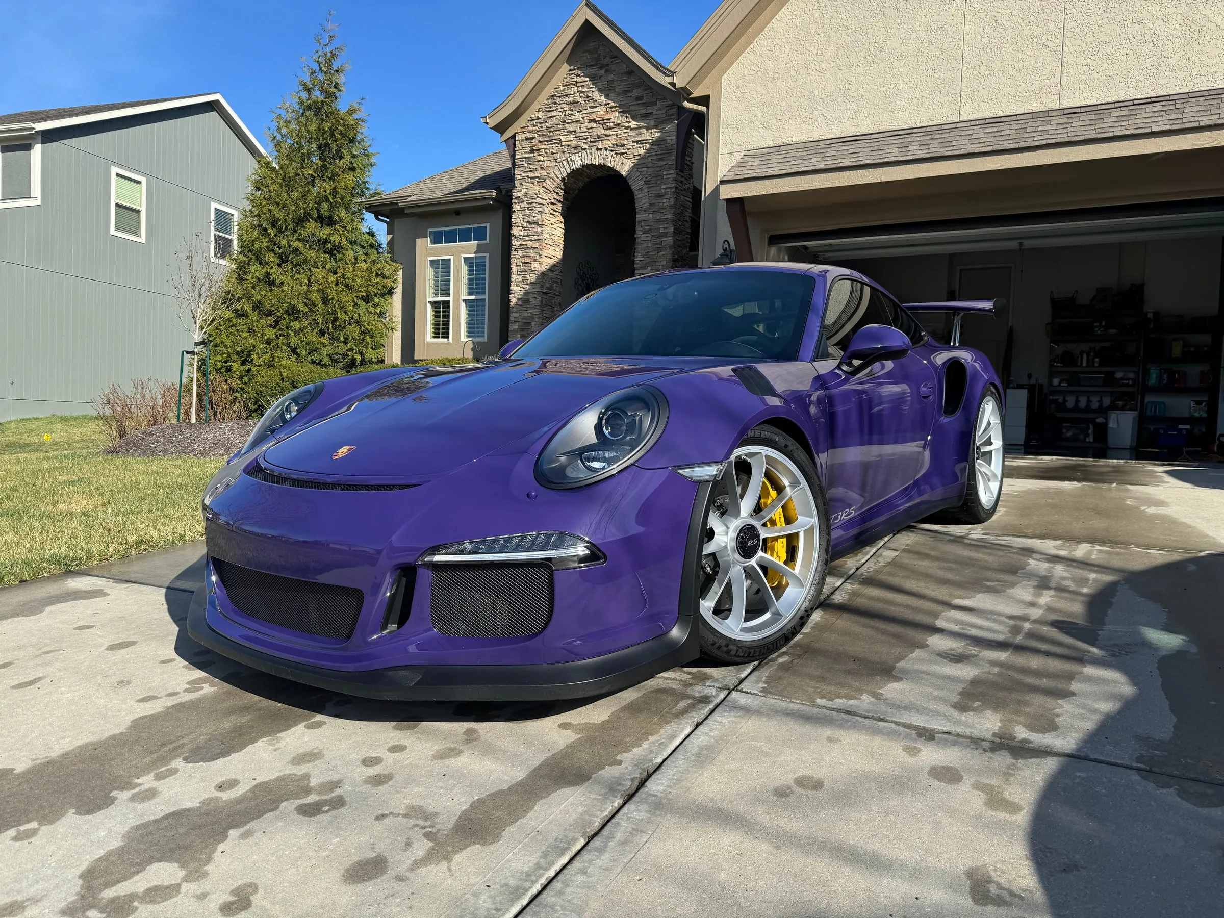 Purple Porsche 911 GT3 RS on a residential driveway, paint reflecting the sky and surrounding houses