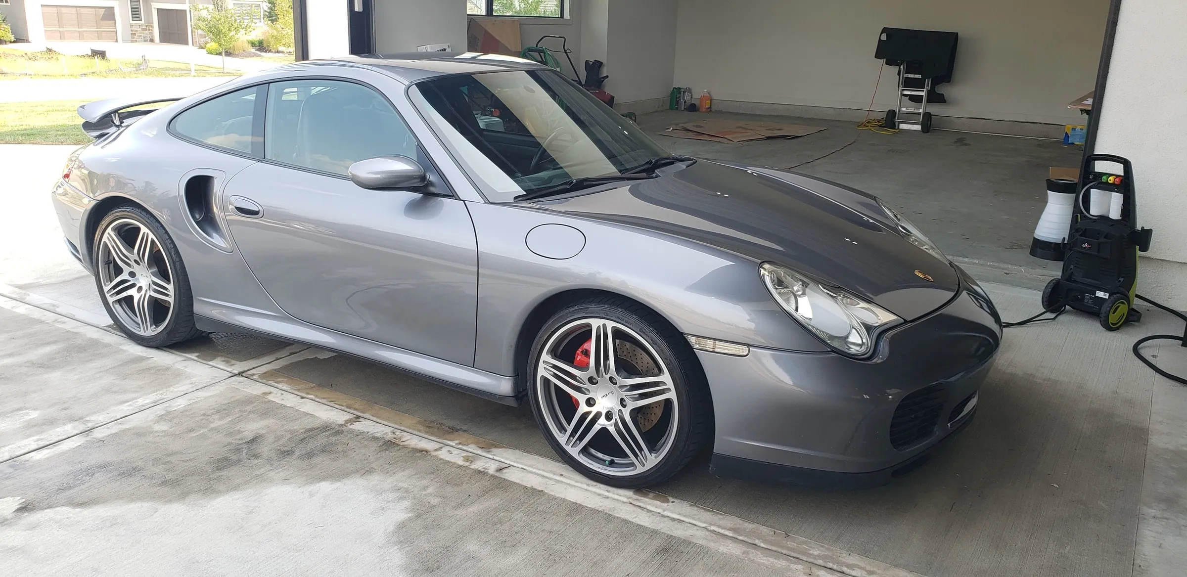 Silver Porsche 911 Turbo at a three-quarter front angle on a driveway, pressure washer still set up beside it