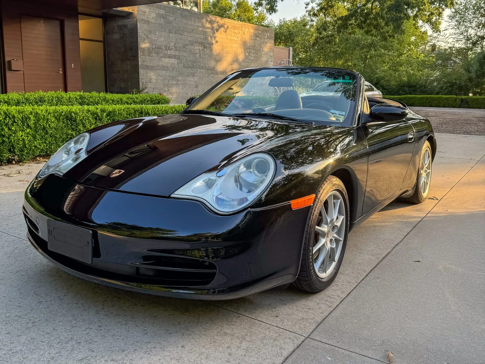 Black Porsche Boxster convertible with the roof down, parked under a covered slab