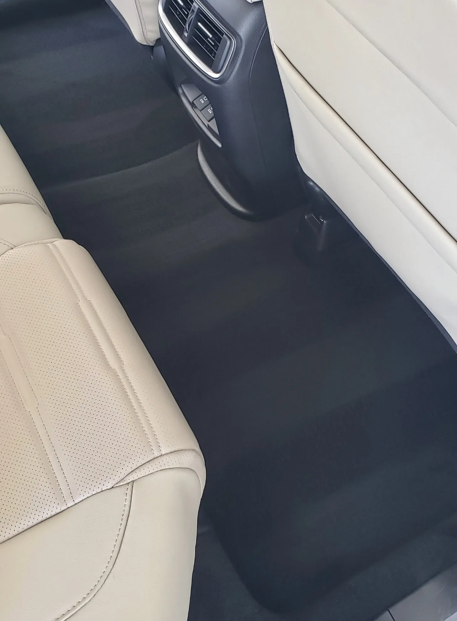 Rear footwell of a car with cream leather seats and dark carpet cleaned and vacuumed in even lines