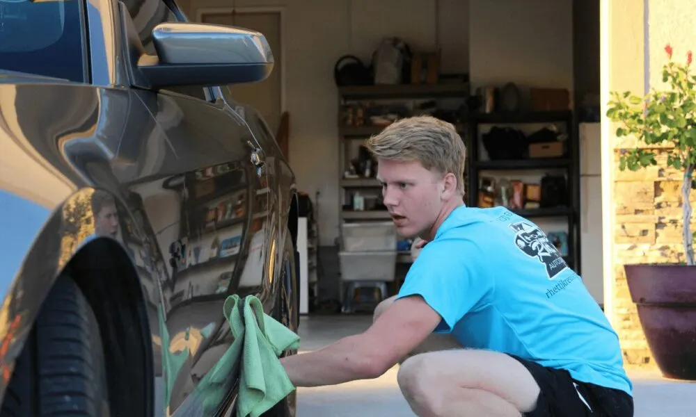 Rhett detailing the door panel of a car, wearing a Rhett's Auto shirt