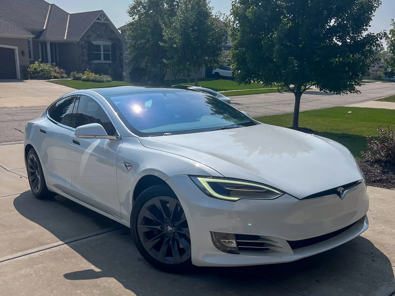 White Tesla Model S on a residential street, paint clean and reflecting the sky