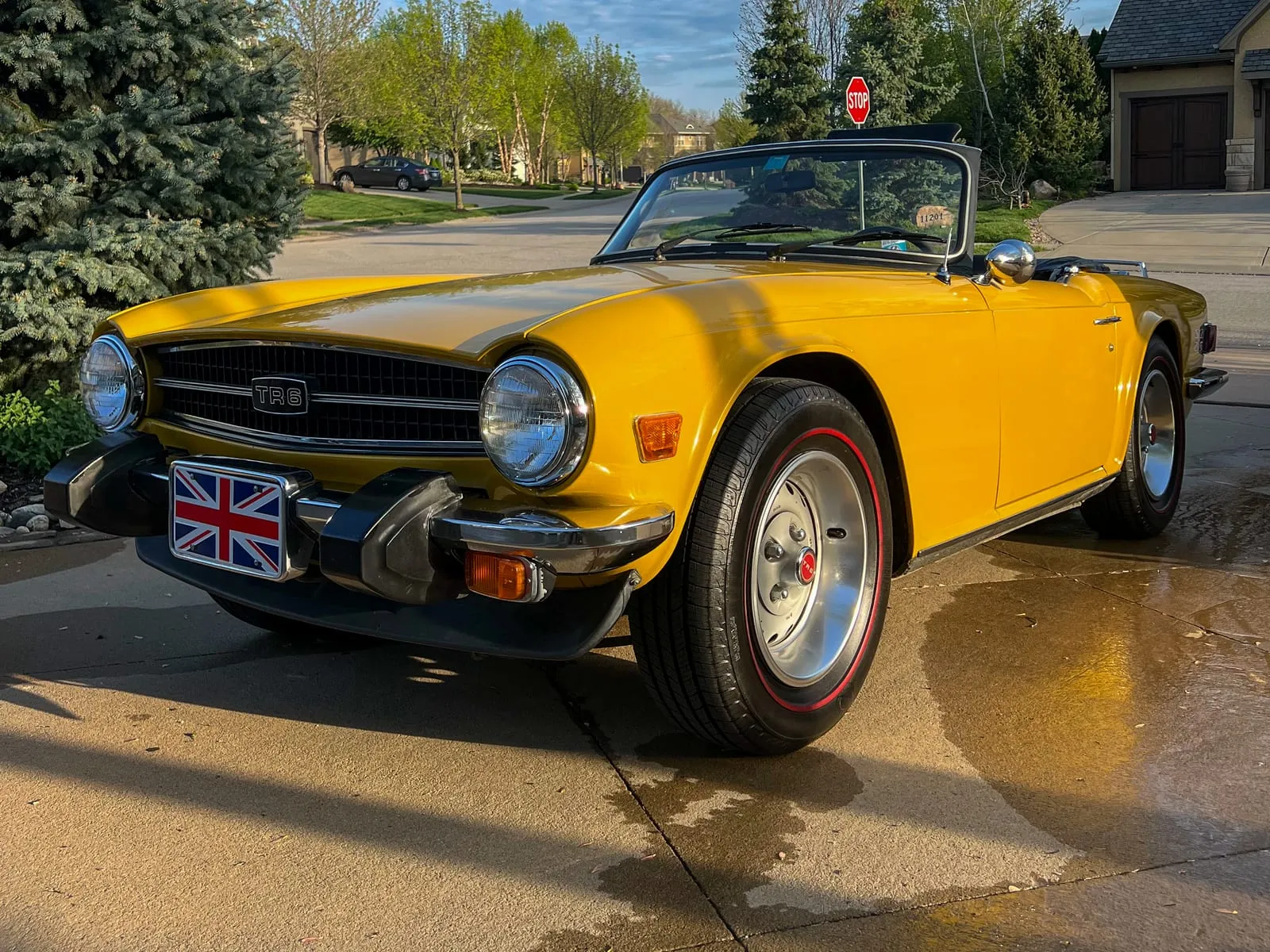 Yellow Triumph TR6 convertible on a wet driveway, chrome bumpers and wire wheels cleaned