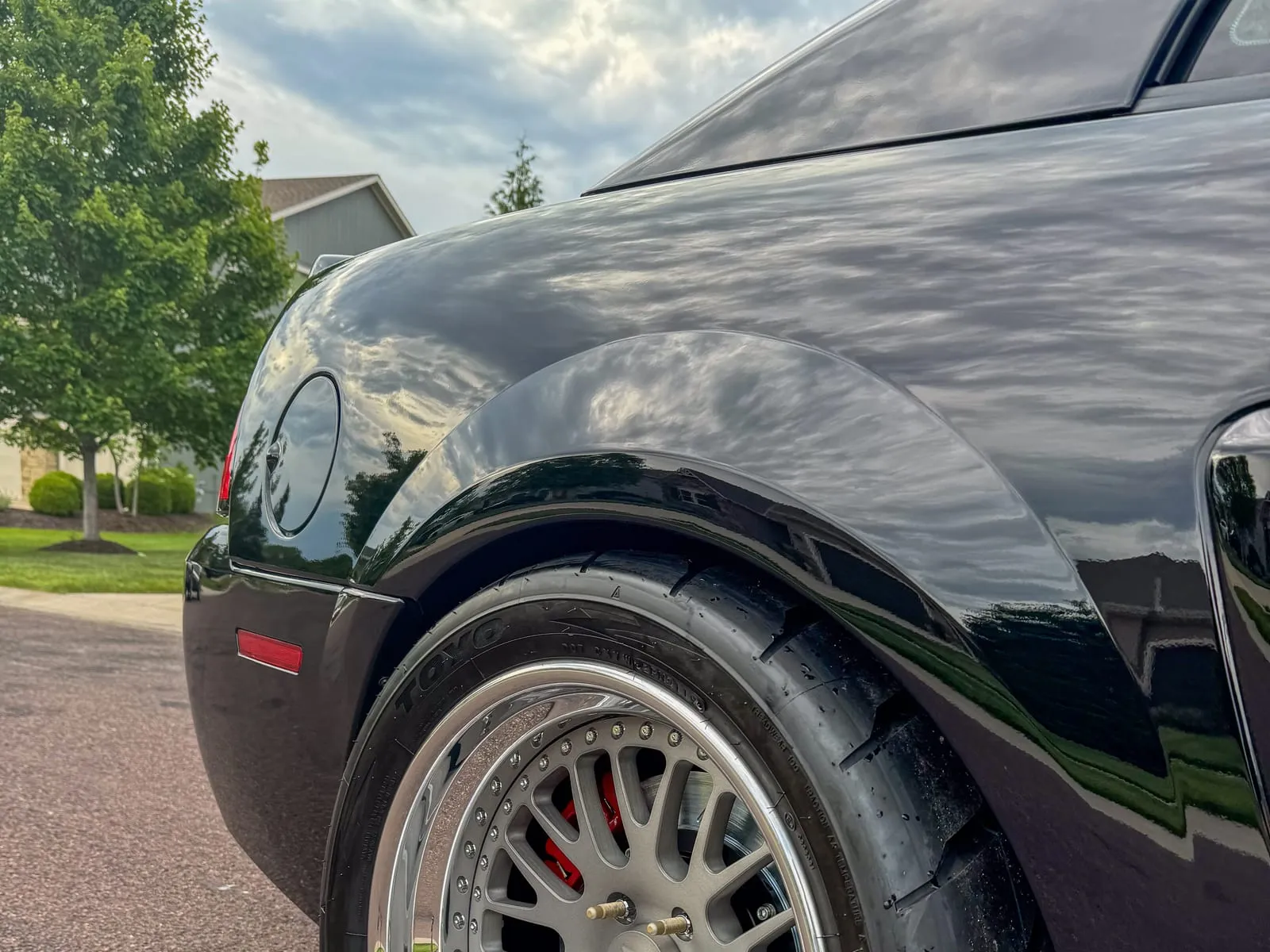 Close view of a polished multi-piece wheel and tire under a black arch, the paint above it clean