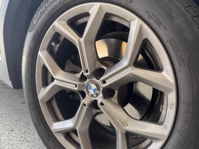 A BMW alloy wheel lying face up on a driveway, the machined face dulled brown with baked-on brake dust